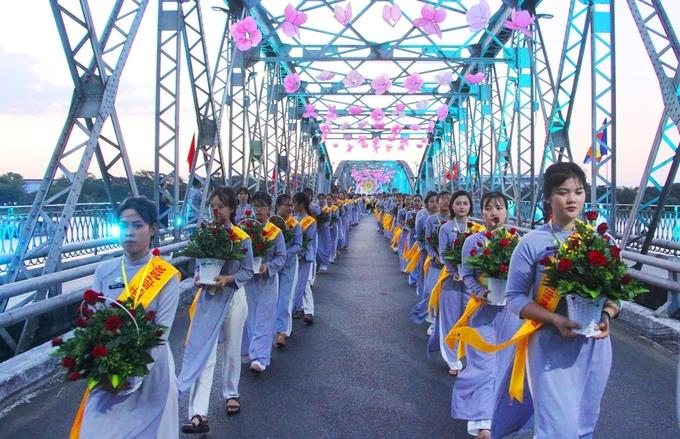 Các nữ phật tử trong tà áo dài màu lam trong đội bưng hoa đi qua cầu Trường Tiền bắc qua dòng sông Hương thơ mộng.